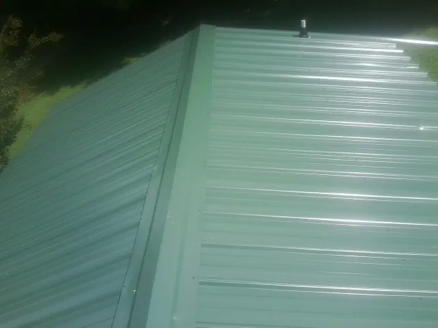 New green metal panels meeting at the ridge of a roof — Flat Roof Repair work by our crew in Russellville